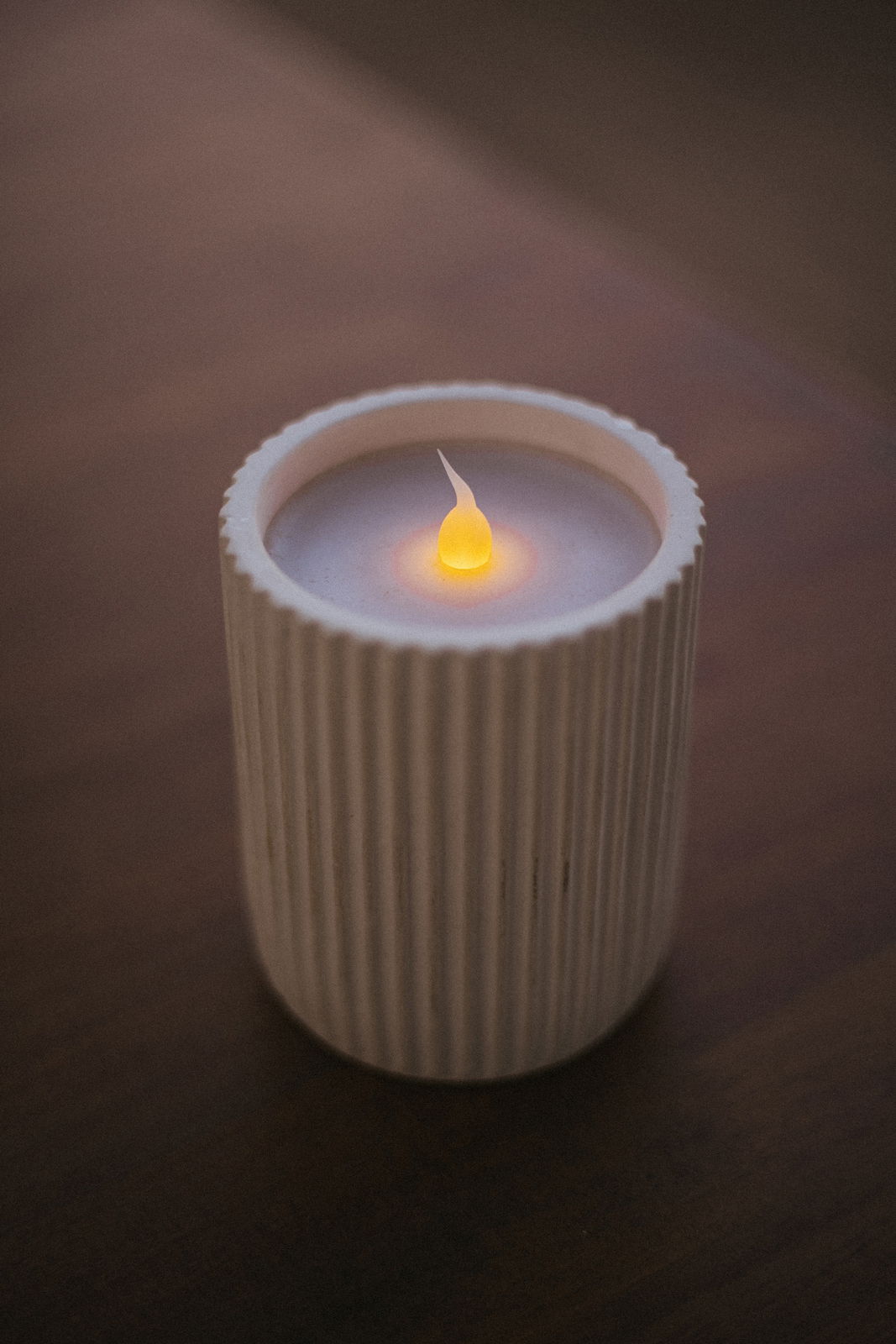 Outdoor-Kerze in einem geriffelten, weißen Behälter, von oben fotografiert, mit einer leuchtenden Flamme.