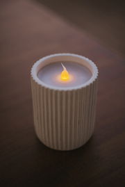 Outdoor-Kerze in einem geriffelten, weißen Behälter, von oben fotografiert, mit einer leuchtenden Flamme.