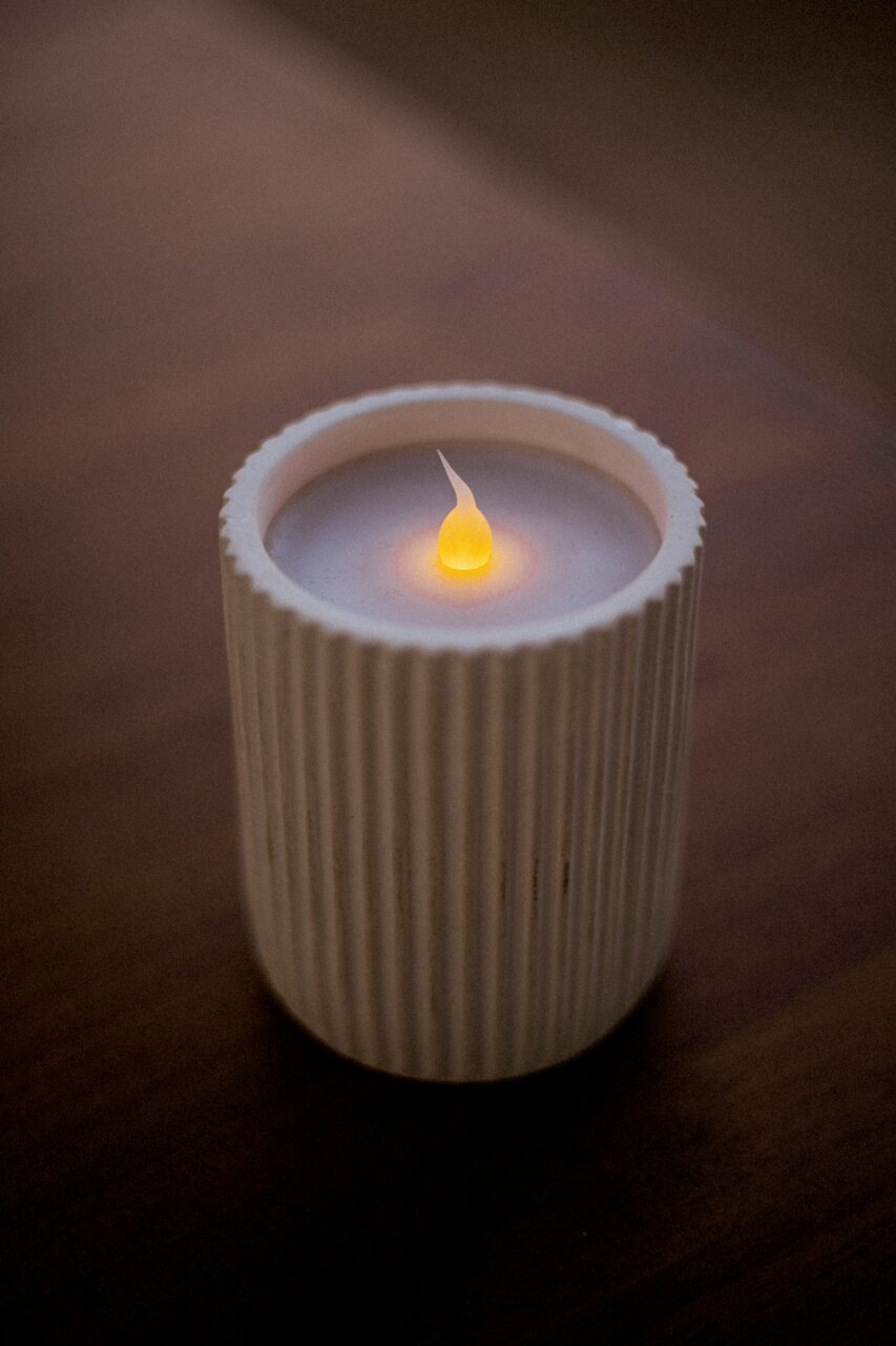 Buitenkaars in een geribbelde, witte houder, van bovenaf gefotografeerd, met een brandende vlam.