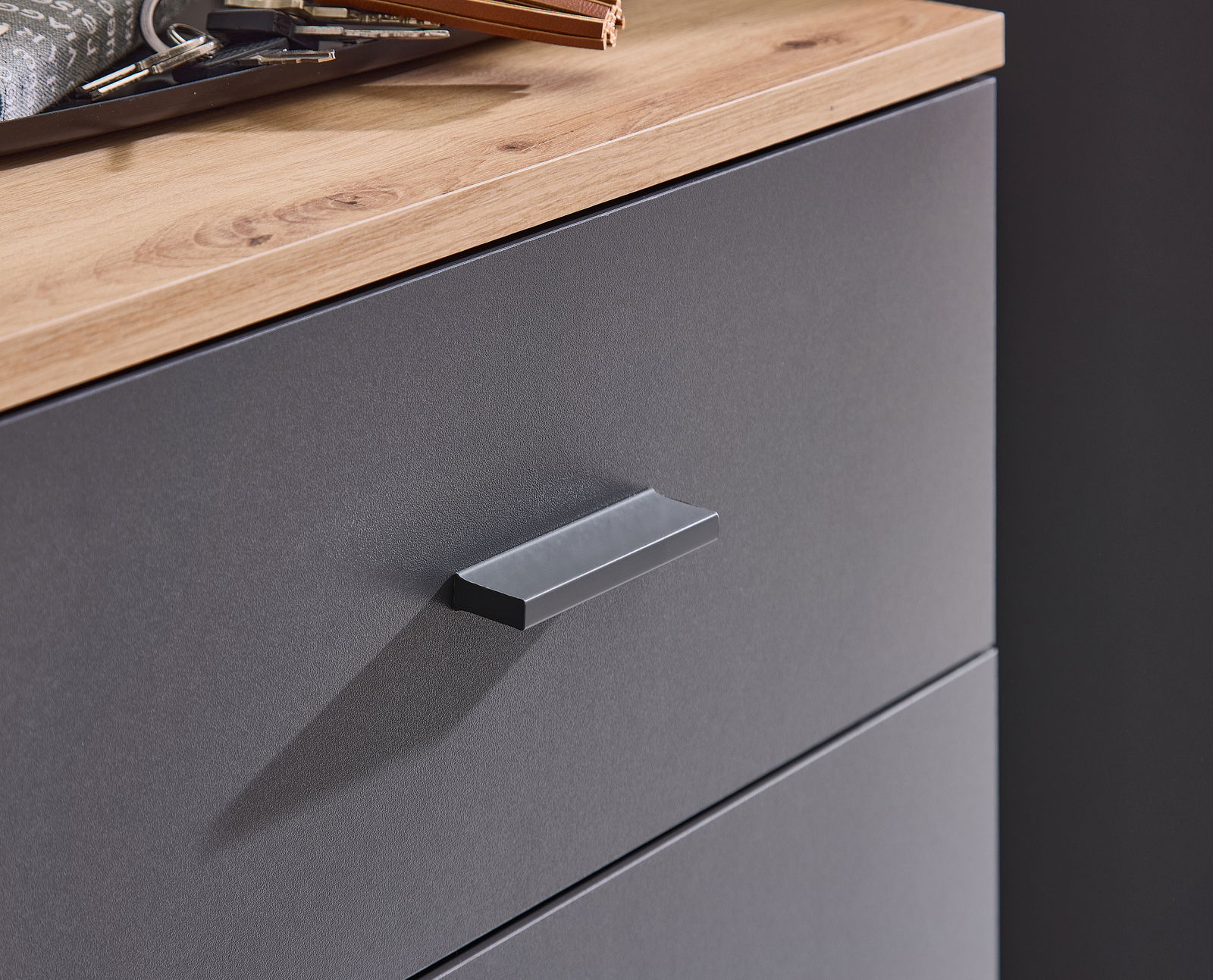 Nahaufnahme einer Kompaktgarderobe mit grauer Schubladenfront und Holzoberfläche, seitliche Perspektive