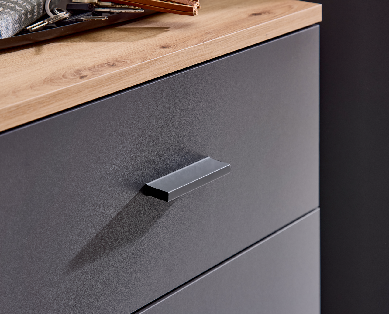 Nahaufnahme einer Kompaktgarderobe mit grauer Schubladenfront und Holzoberfläche, seitliche Perspektive