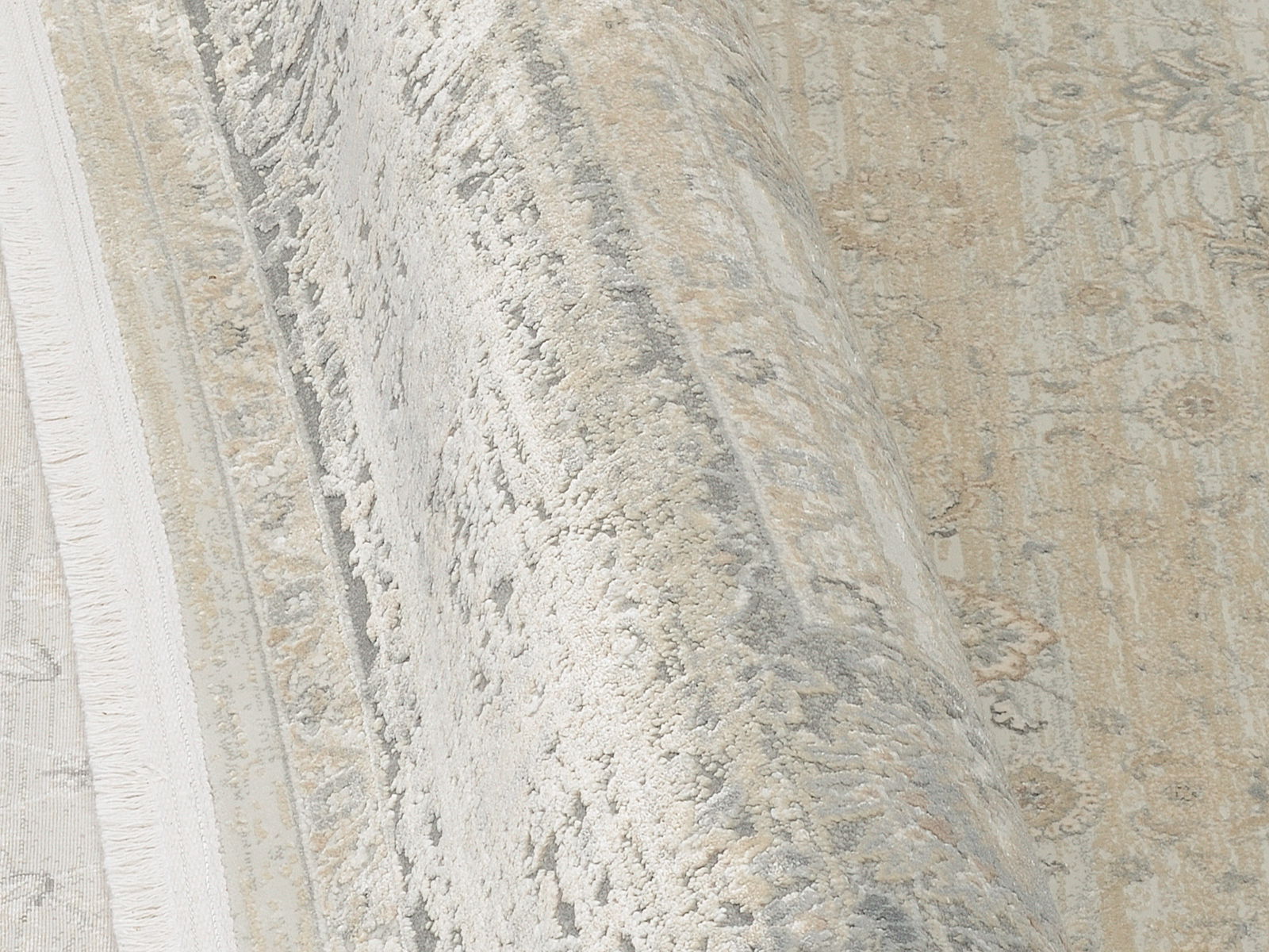 Nahaufnahme eines Designer-Teppichs mit floralen Mustern in Beige- und Grautönen, perspektivisch von der Seite aufgenommen.