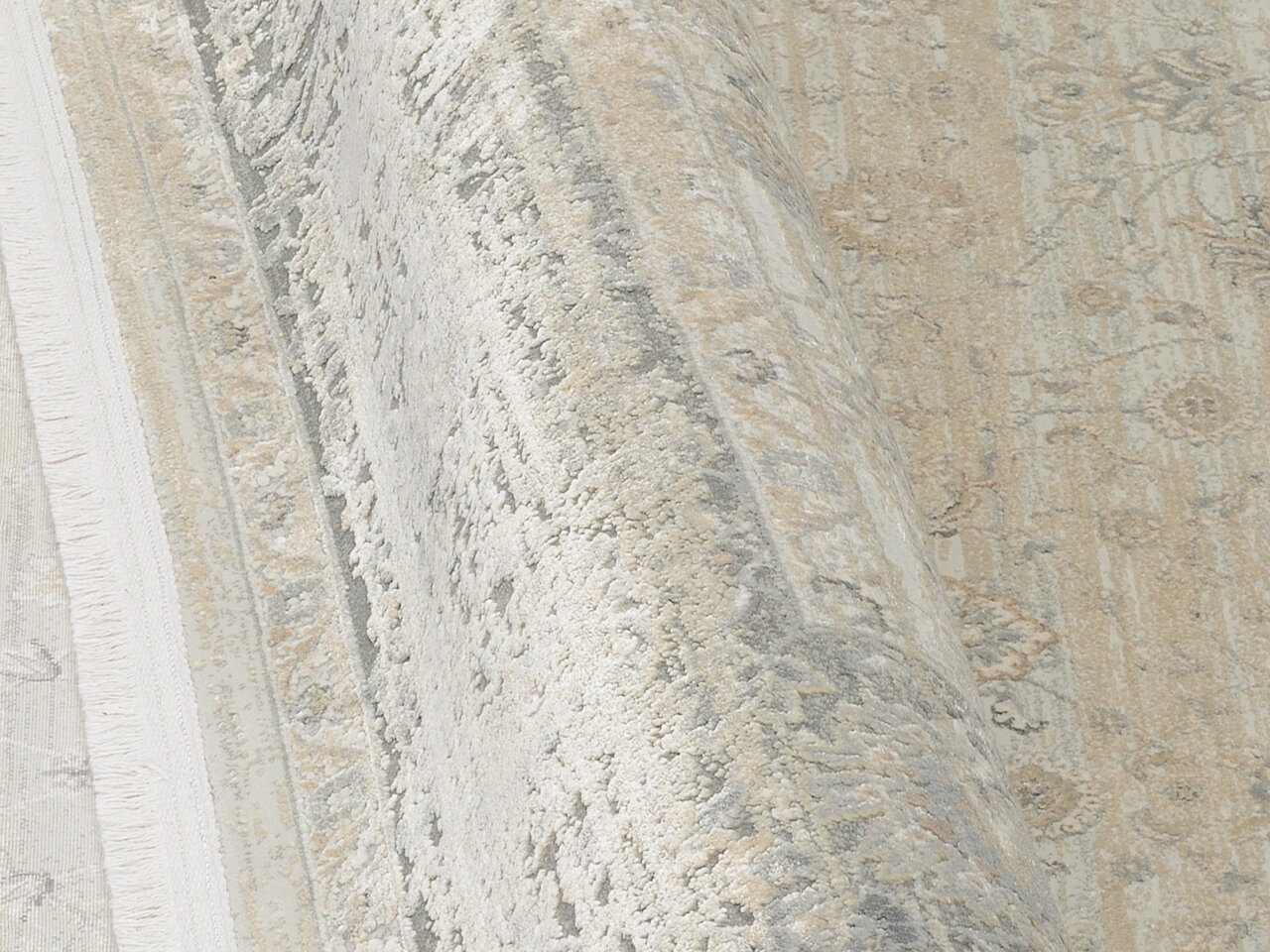 Nahaufnahme eines Designer-Teppichs mit floralen Mustern in Beige- und Grautönen, perspektivisch von der Seite aufgenommen.