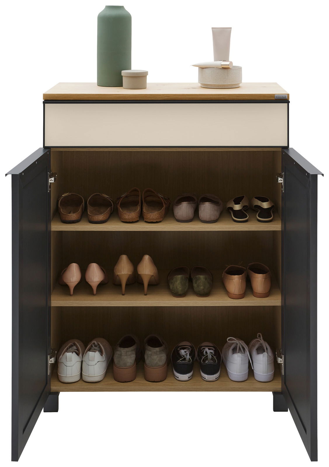 Schuhschrank mit geöffneter Tür, gefüllt mit verschiedenen Schuhen auf drei Regalböden, aus der Frontalperspektive fotografiert. Oben auf dem Schrank stehen dekorative Gegenstände.