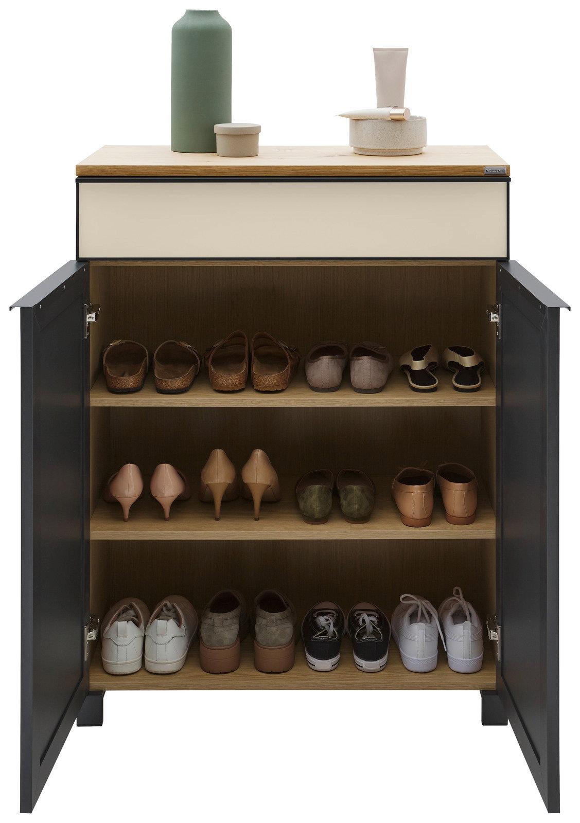 Schuhschrank mit geöffneter Tür, gefüllt mit verschiedenen Schuhen auf drei Regalböden, aus der Frontalperspektive fotografiert. Oben auf dem Schrank stehen dekorative Gegenstände.