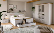 Modernes Schlafzimmer mit weißem Holzbett und ausziehbarer Bettkasten-Schublade, Nachttisch und großem Kleiderschrank mit Spiegeltüren; Ansicht schräg von vorn.