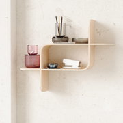 Modernes Wandregal aus hellem Holz mit geschwungenem Design, dekoriert mit farbigen Gläsern und Büroartikeln, seitliche Perspektive.