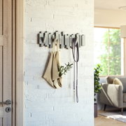 Moderne houten wandkapstok met een geometrisch ontwerp, aan de voorkant bevestigd aan een witte bakstenen muur, met een opgehangen tas en een waslijn.
