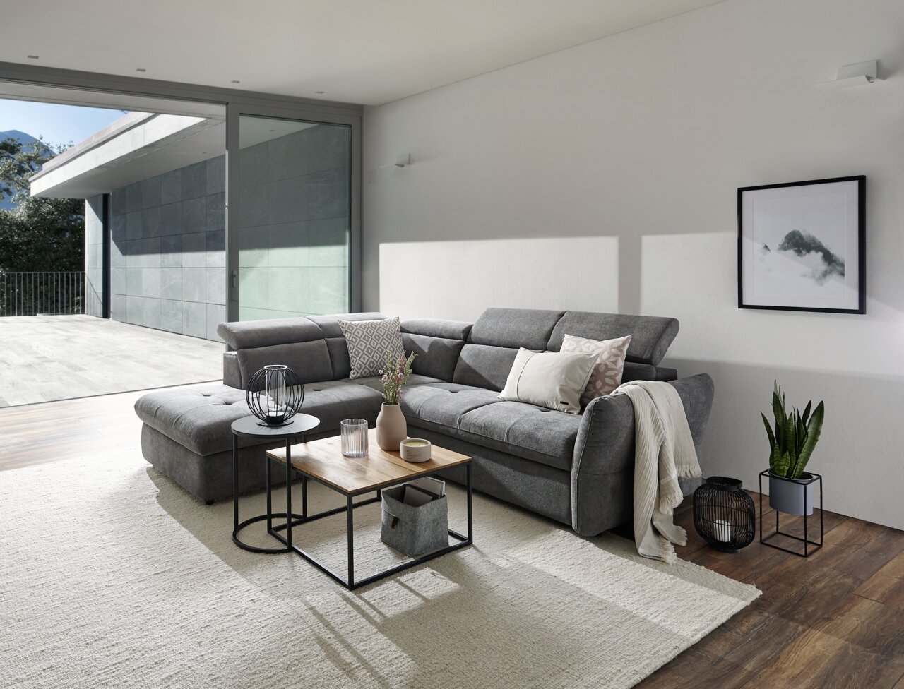 Stylife Ecksofa MONSERAT Graue Polsterrundecke in modernem Wohnzimmer, seitliche Perspektive mit Blick auf großen Fensterbereich.