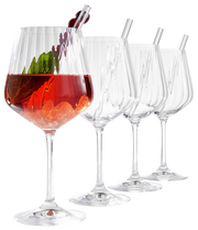 Vier elegante Gin Tonic-Gläser, eines davon gefüllt mit einem roten Getränk, Eis und einer Garnitur, aus seitlicher Perspektive fotografiert.