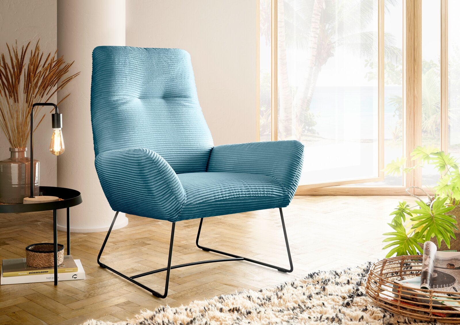 Lounge Handmade Fauteuil LH-BEN Moderne blauwe fauteuil met geribbelde stoffen bekleding, gezien vanaf de zijkant, in een lichte ruimte met grote ramen en planten.