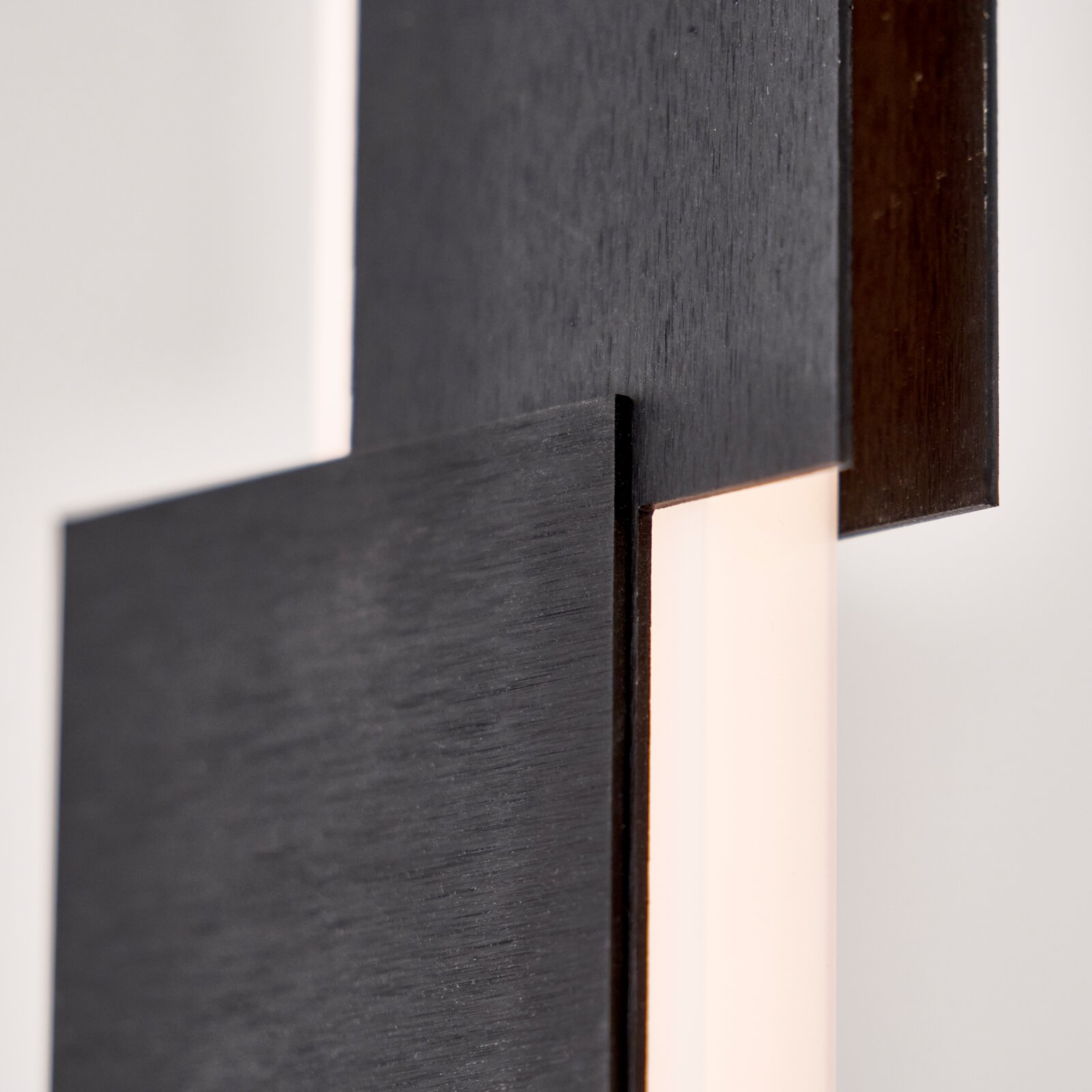 Detailansicht aus seitlicher Nahperspektive einer modernen Leuchte mit überlappenden, dunkel gebürsteten Metallflächen und warm leuchtendem Diffusor