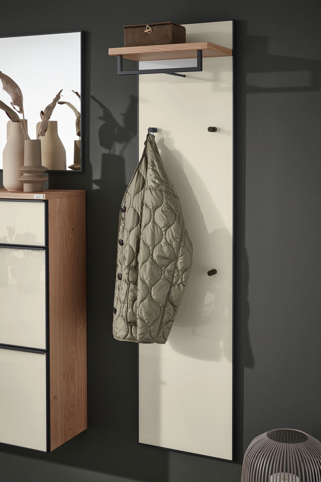 Garderobenpaneel mit einem hängenden Mantel, einem Regalbrett oben und einer modernen, minimalistischen Gestaltung. Seitliche Perspektive.