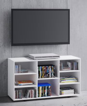 Weißes TV-Lowboard/Medienregal mit offenen Fächern, gefüllt mit DVDs, CDs und Zeitschriften; oben ein DVD-Player, darüber ein wandmontierter Flachbildfernseher vor Betonwand, Frontansicht.