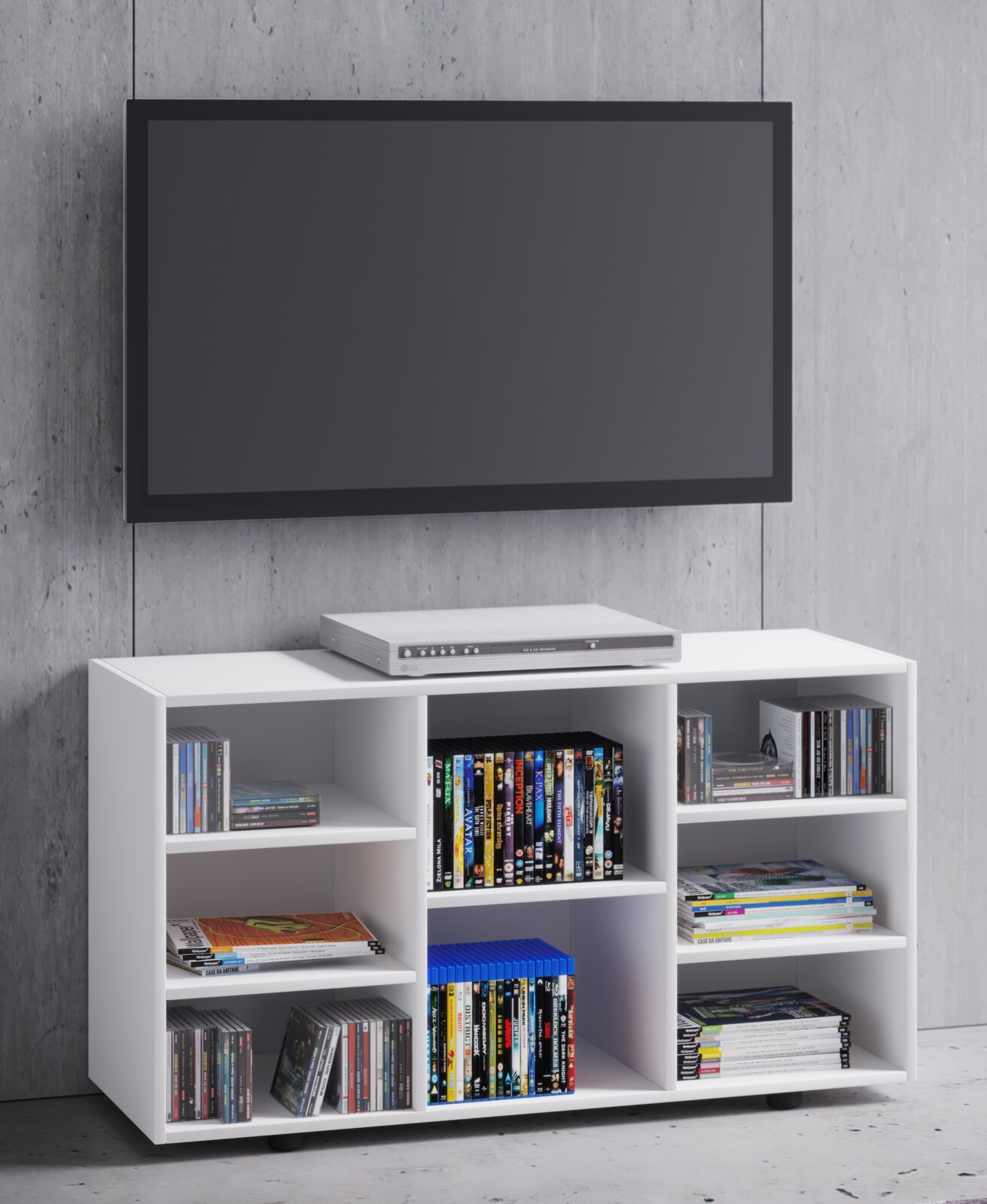 Weißes TV-Lowboard/Medienregal mit offenen Fächern, gefüllt mit DVDs, CDs und Zeitschriften; oben ein DVD-Player, darüber ein wandmontierter Flachbildfernseher vor Betonwand, Frontansicht.
