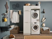 Hauswirtschaftsraum mit Waschmaschine und Trockner in einem weißen Hochschrank, umgeben von Körben und Hängeregalen, seitliche Perspektive.