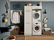 Hauswirtschaftsraum mit Waschmaschine und Trockner in einem weißen Hochschrank, umgeben von Körben und Hängeregalen, seitliche Perspektive.