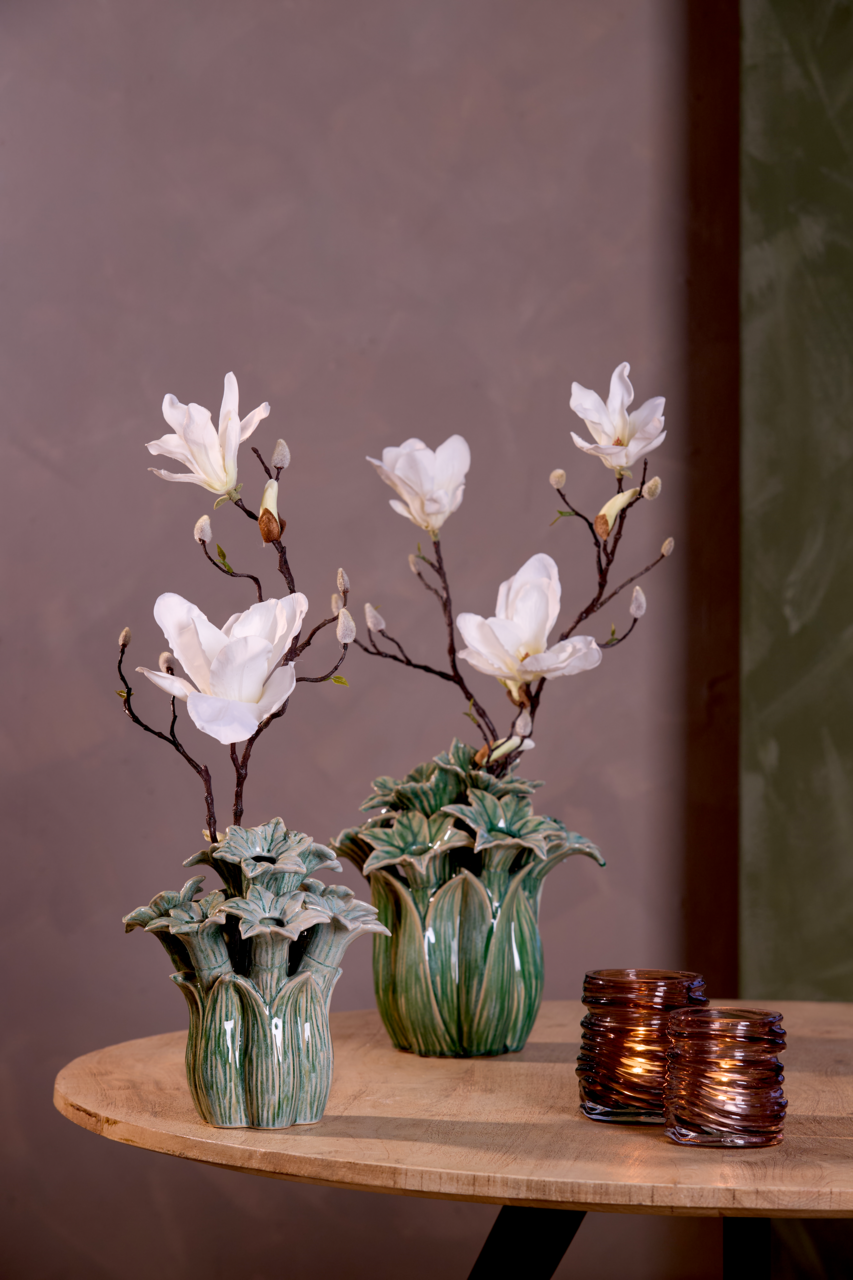 Zwei grüne Vasen mit weißen Blumen und zwei braune Teelichthalter auf einem Holztisch, seitliche Perspektive.