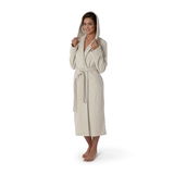 Frau in einem beigen Kapuzenbademantel, stehend in Frontalansicht, mit Kapuze aufgesetzt und Gürtel gebunden.