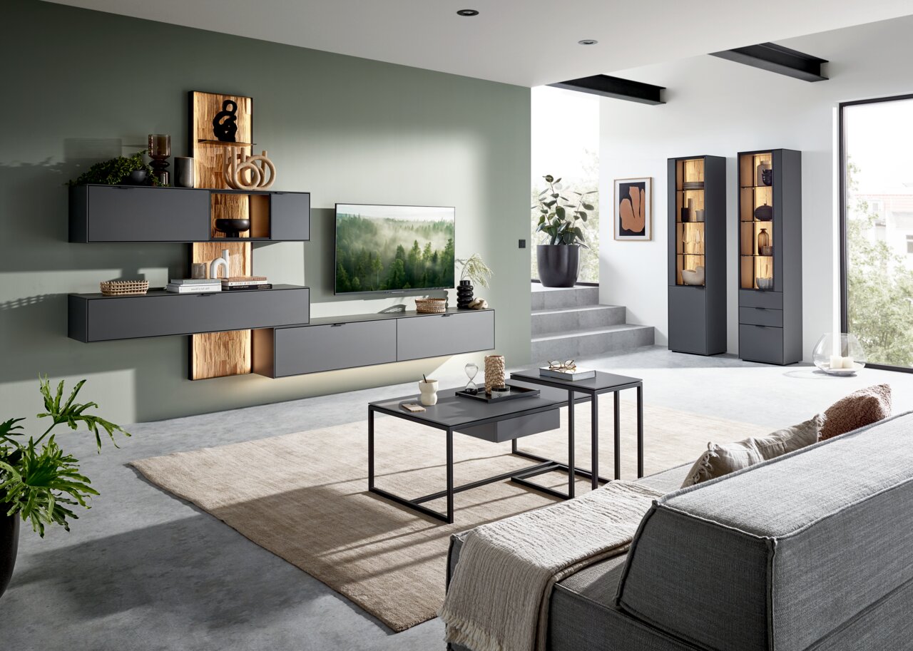 Moderne Wohnzimmer-Wandkombination in dunklem Grau mit Holzakzenten, stilvoll dekoriert, aus der Perspektive eines gemütlichen Wohnzimmers mit Sofa und Couchtischen.