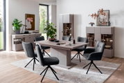 Modernes Esszimmer-Set mit rechteckigem Esstisch in Taupe/Grau und sechs gepolsterten, dunkelgrauen Drehstühlen auf gemustertem Teppich, umgeben von Sideboard und Vitrine – Perspektive: leicht erhöhte Frontansicht schräg von links.