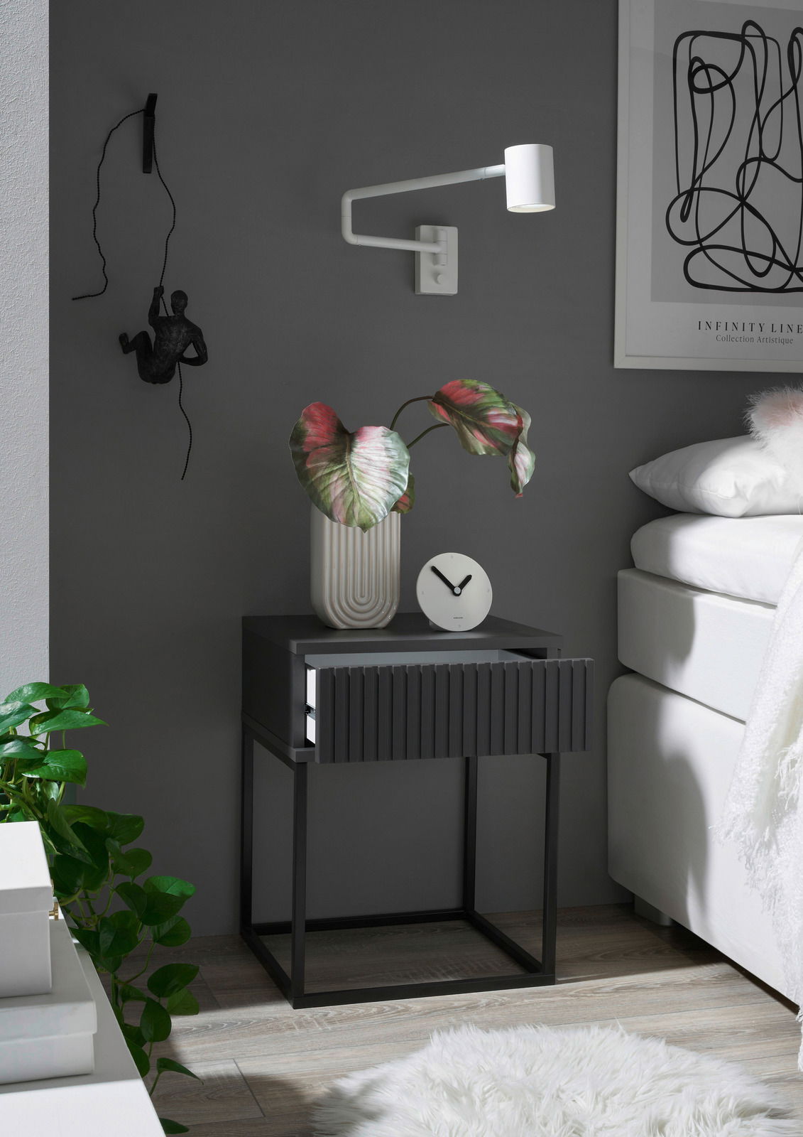 Moderne Nachtkommode in dunklem Design mit geriffelter Schubladenfront, dekoriert mit einer Pflanze und einer Uhr, seitliche Perspektive