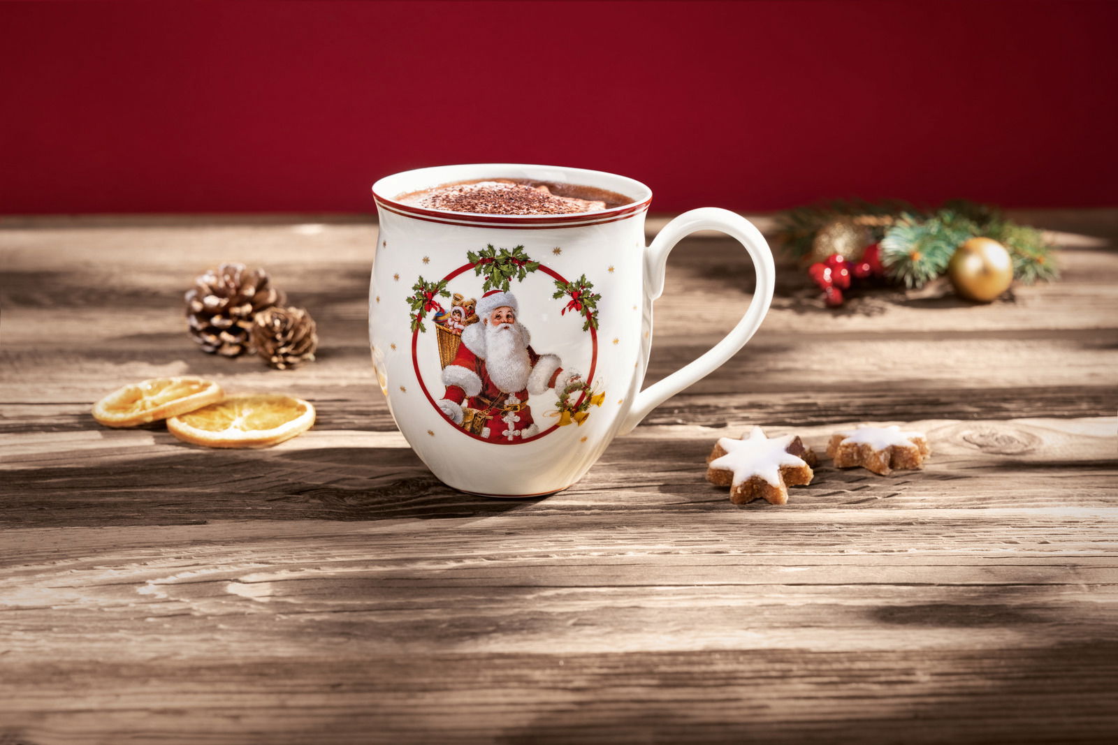Weihnachtsbecher mit Weihnachtsmann-Motiv, gefüllt mit heißer Schokolade, auf einem Holztisch mit weihnachtlicher Dekoration, seitliche Perspektive