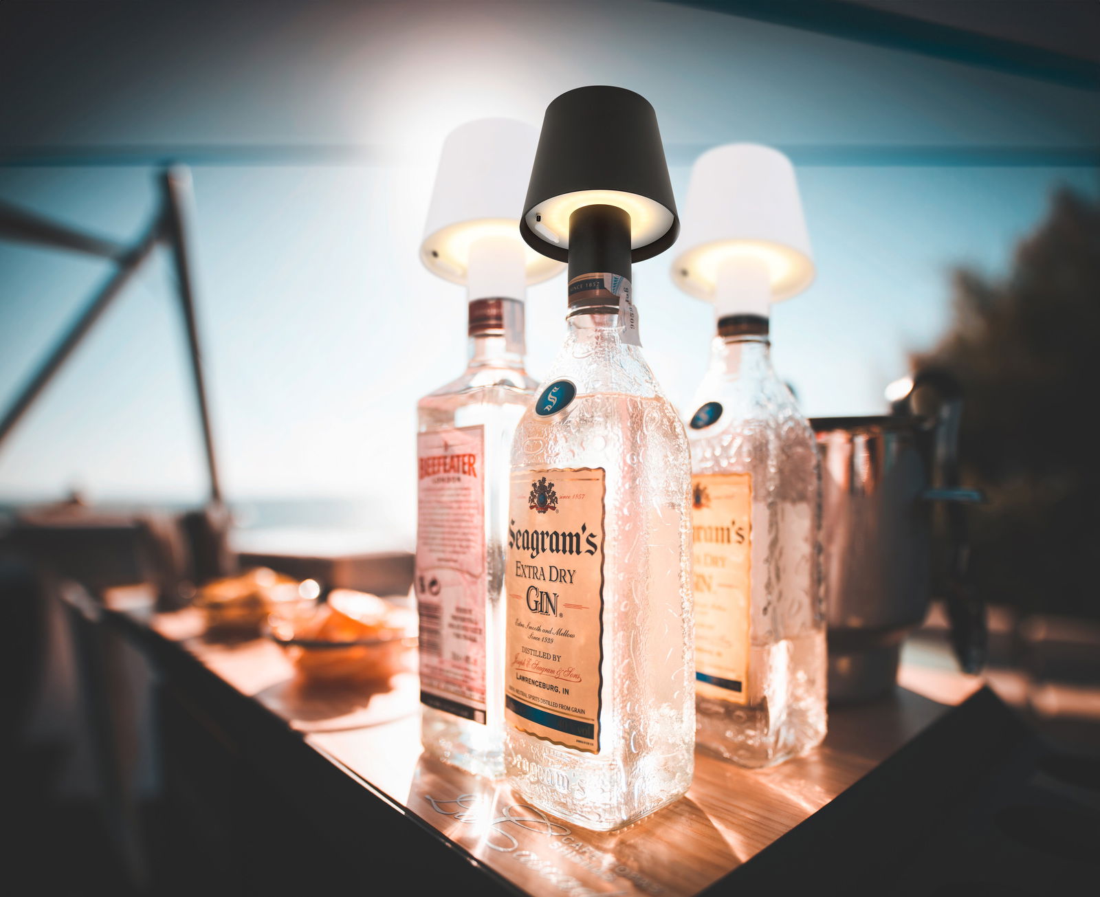 Akku-Aufsatzleuchte VANNIE auf einer Flasche, seitliche Perspektive, im Freien bei Tageslicht.