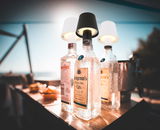 Akku-Aufsatzleuchte VANNIE auf einer Flasche, seitliche Perspektive, im Freien bei Tageslicht.