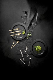 Vogelperspektive auf ein stilvolles Besteckset mit goldenen und silbernen Besteckteilen, arrangiert auf dunklen Tellern mit grüner Dekoration.