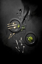 Vogelperspektive auf ein stilvolles Besteckset mit goldenen und silbernen Besteckteilen, arrangiert auf dunklen Tellern mit grüner Dekoration.