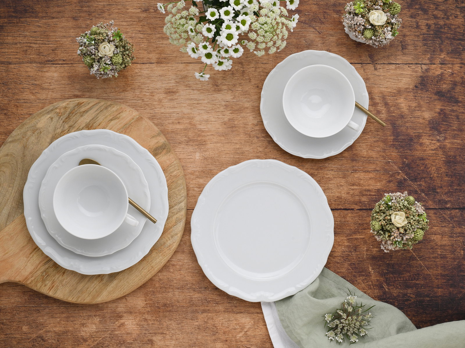 Kaffeeservice 18-tlg aus weißem Porzellan, bestehend aus Tassen, Untertassen und Tellern, auf einem Holztisch von oben fotografiert, dekoriert mit kleinen Blumenarrangements.