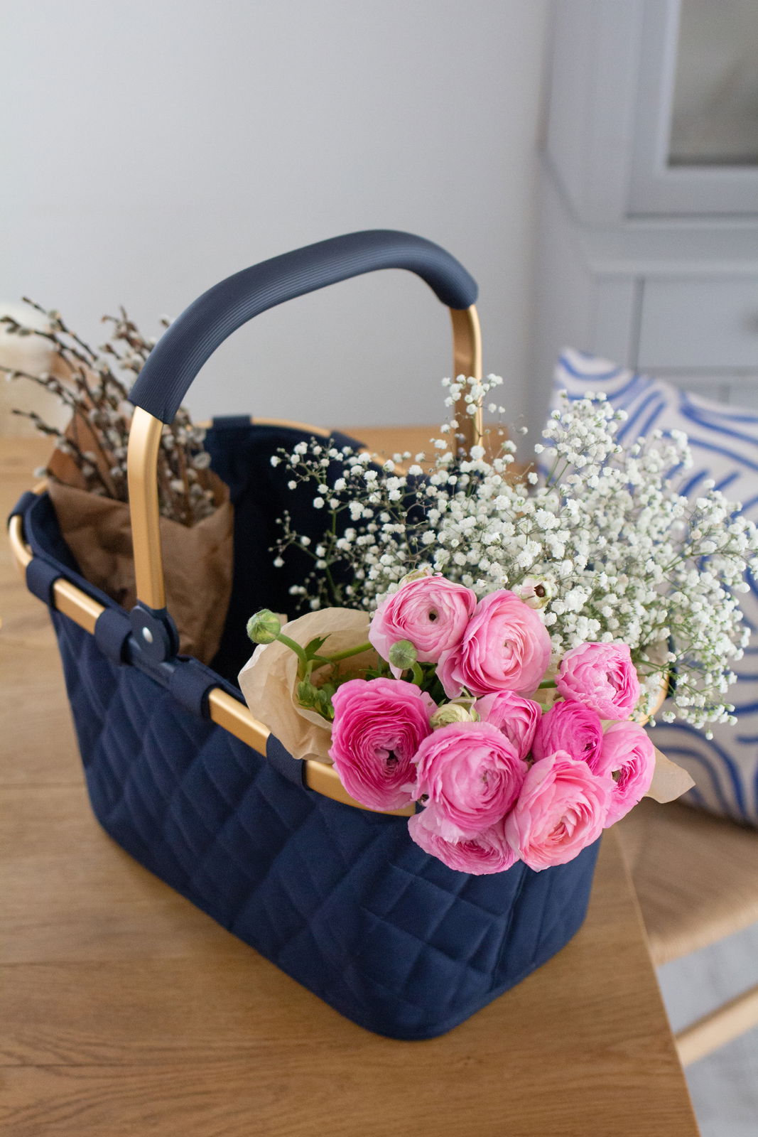 Reisenthel Carrybag Frame Rhombus Midnight Tragetasche mit Rhombus-Muster in Mitternachtsblau, gefüllt mit Blumen, auf einem Tisch von schräg oben fotografiert.