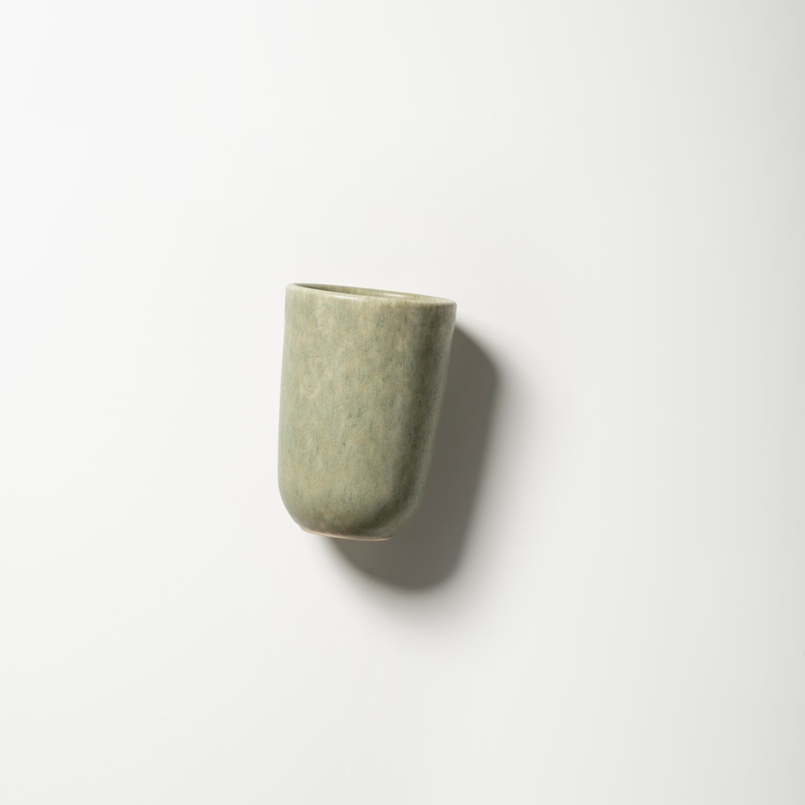 Hellgrüner, leicht konischer Keramikbecher mit matter Oberfläche auf weißem Hintergrund, schräg von oben fotografiert (Draufsicht)