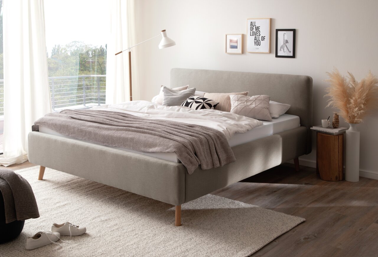Modernes Polsterbett in einem hellen Schlafzimmer, seitliche Perspektive, mit dekorativen Kissen und Decken.