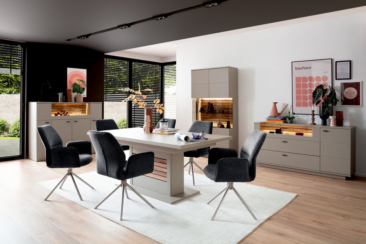 Zurbrüggen Esstisch LÜTTICH Moderne Esszimmermöbel mit Esstisch, Stühlen und Sideboards in einem hellen Raum mit großen Fenstern, seitliche Perspektive.