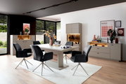 Moderne Esszimmermöbel mit Esstisch, Stühlen und Sideboards in einem hellen Raum mit großen Fenstern, seitliche Perspektive.