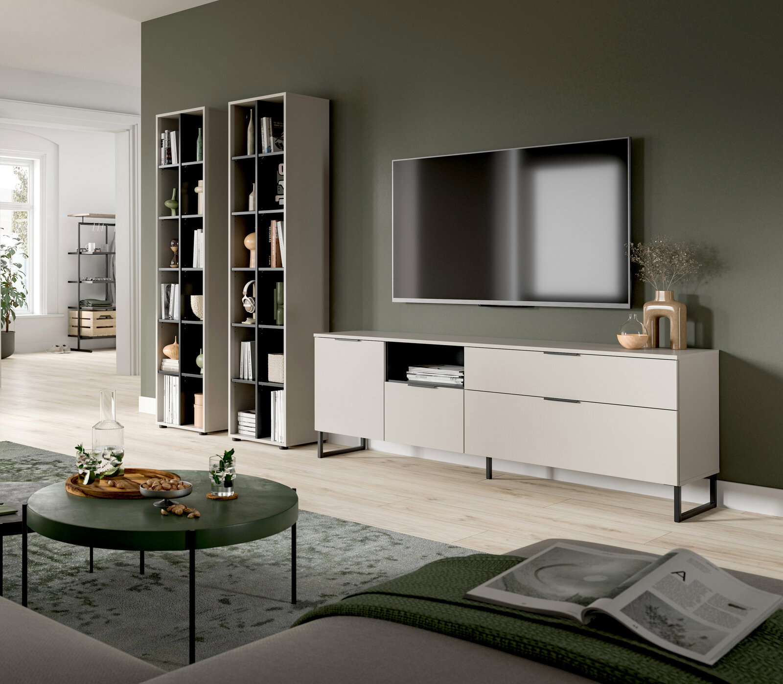 Modernes Wohnzimmer-Setup mit weißem TV-Lowboard auf schwarzen Metallfüßen, zwei hohen offenen Regalen und wandmontiertem Fernseher vor olivgrüner Wand, aufgenommen in schräger Frontansicht aus leicht erhöhter Perspektive.