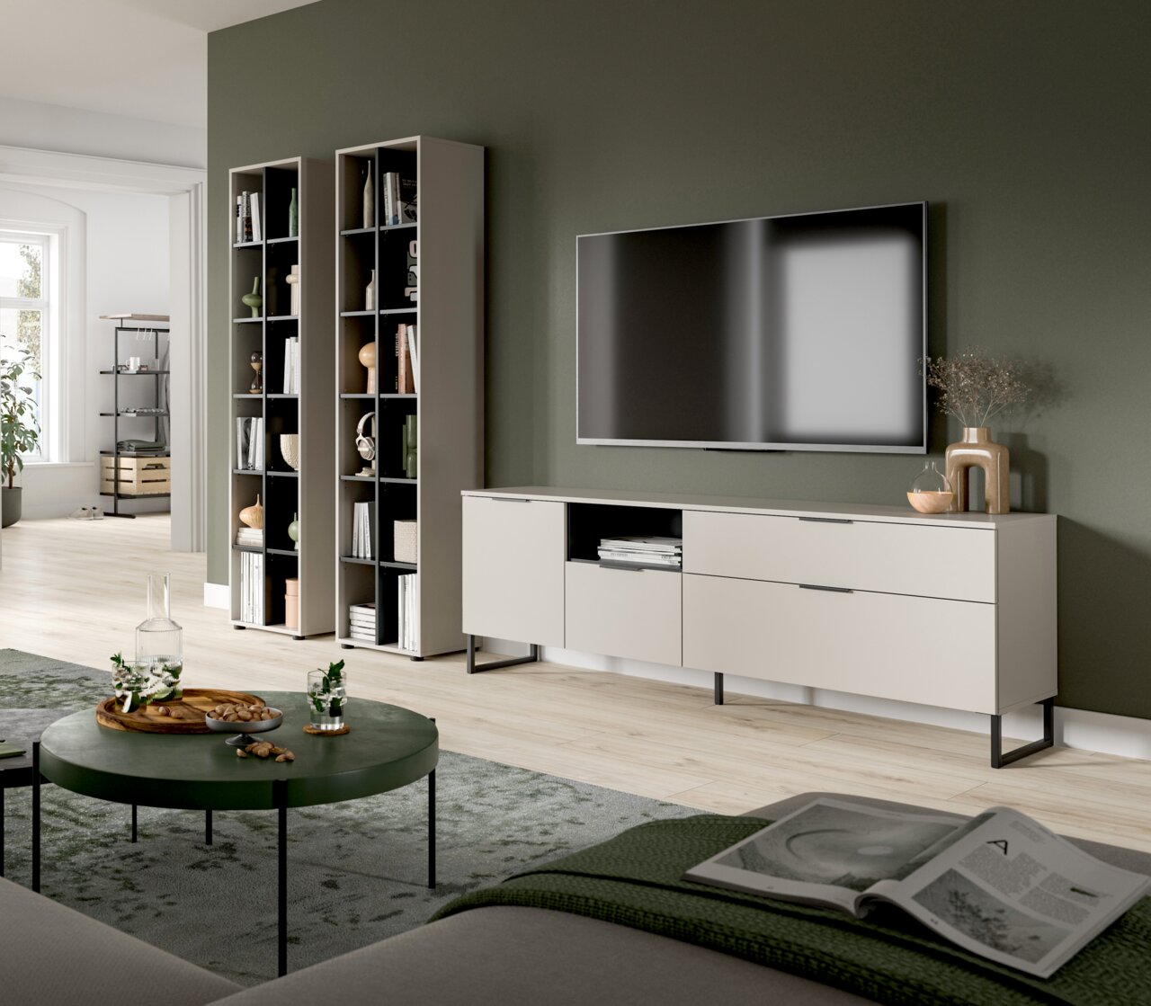 MID.YOU Wohnkombination NOIDA Modernes Wohnzimmer-Setup mit weißem TV-Lowboard auf schwarzen Metallfüßen, zwei hohen offenen Regalen und wandmontiertem Fernseher vor olivgrüner Wand, aufgenommen in schräger Frontansicht aus leicht erhöhter Perspektive.