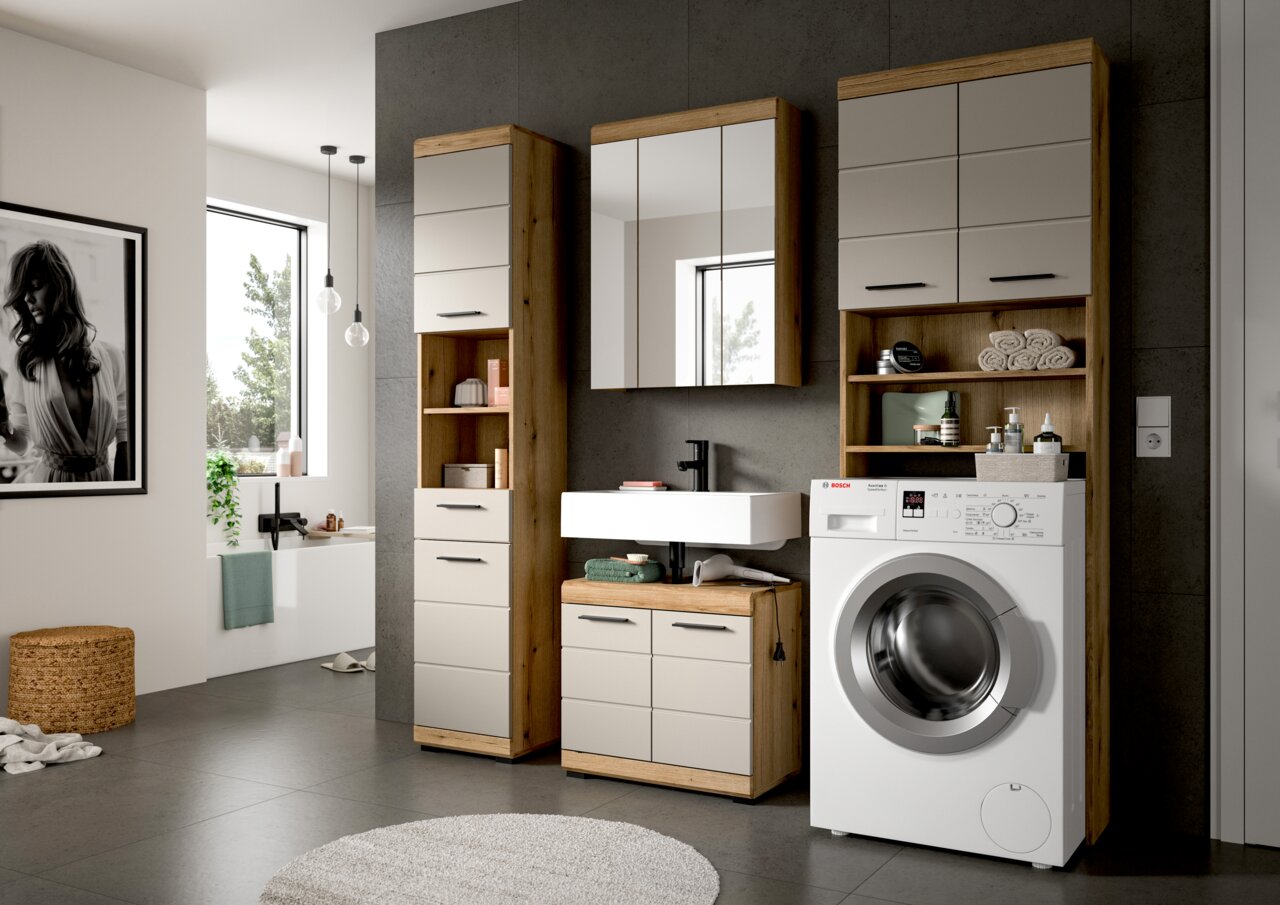 Modernes Badmöbel-Set in Holzoptik mit hellen Fronten, bestehend aus Hochschrank, Spiegelschrank und Waschtischunterschrank mit Aufsatzwaschbecken; daneben Waschmaschine und Regal – Frontansicht in leichter Schrägperspektive.
