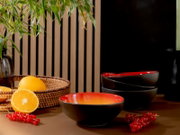 Drei schwarze Keramikschalen mit leuchtend roter Innenglasur, aus leicht erhöhter Frontalperspektive neben Orangen und roten Johannisbeeren arrangiert
