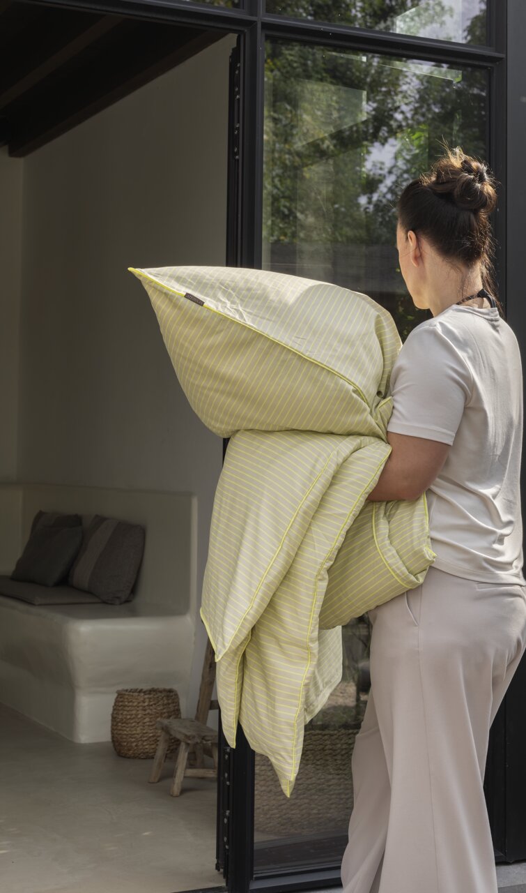 Een persoon draagt geelgestreept beddengoed in een moderne, lichte kamer.