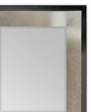 Nahaufnahme eines Wandspiegels mit einem eleganten, silbernen Rahmen und schwarzem Rand, perspektivisch von der Ecke aufgenommen.