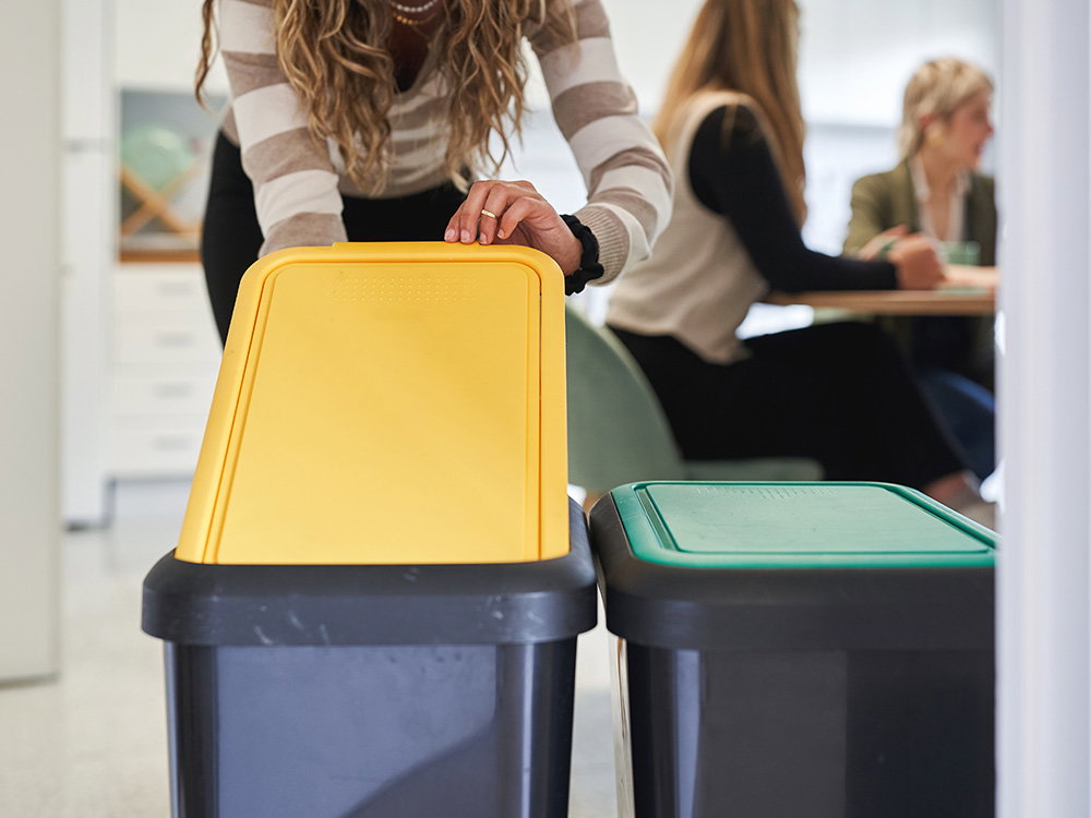 Mitarbeiterin trennt Abfall in Recyclingbehältern im Büro