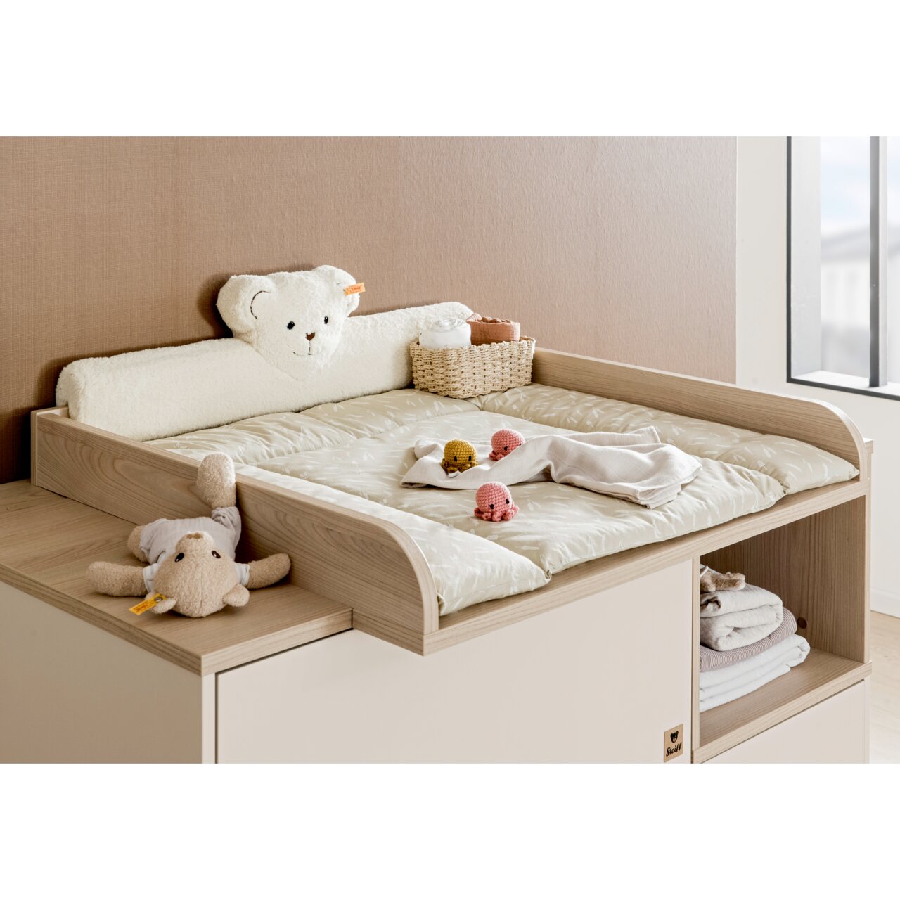 Wickelaufsatz aus Holz mit weicher Wickelauflage, Kuscheltieren und Körbchen, seitliche Perspektive