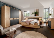 Modernes Schlafzimmer mit Holz- und Schwarzakzenten, bestehend aus einem großen Kleiderschrank, einem Bett mit integrierten Schubladen und zwei Nachttischen, aus der Perspektive von der Zimmerecke aus gesehen.