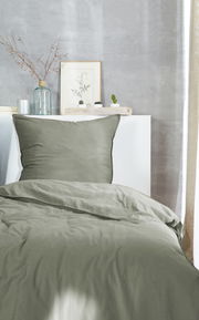 Grüne Bettwäsche 135x200cm auf einem Bett, fotografiert aus der Vorderansicht, mit dekorativen Elementen im Hintergrund.