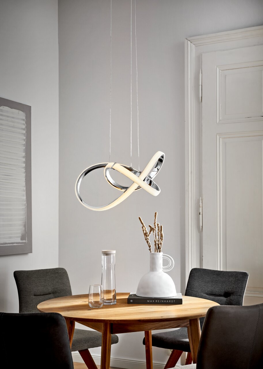 Moderne LED-Hängeleuchte in geschwungenem Design über einem runden Esstisch, seitliche Perspektive.