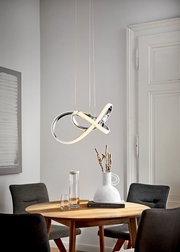 Moderne LED-Hängeleuchte in geschwungenem Design über einem runden Esstisch, seitliche Perspektive.