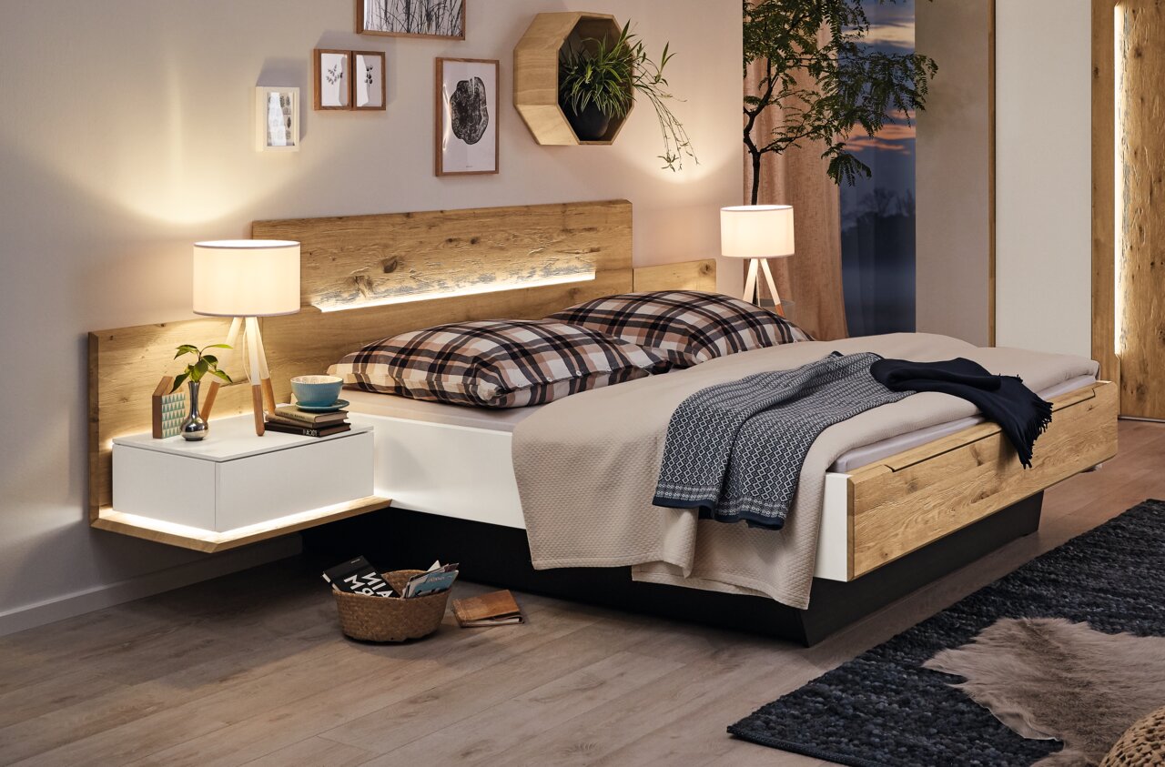 Komfortbett aus Holz mit integrierten Nachttischen, seitlicher Perspektive, dekoriert mit Kissen und Decken in einem gemütlichen Schlafzimmer.